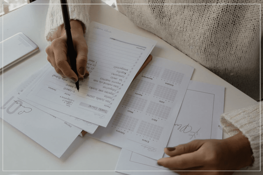 Produtividade não é ter uma checklist cheia de tarefas. Pessoa sentada à mesa com alguns papeis à sua frente e escrevendo em uma lista com muitas tarefas.