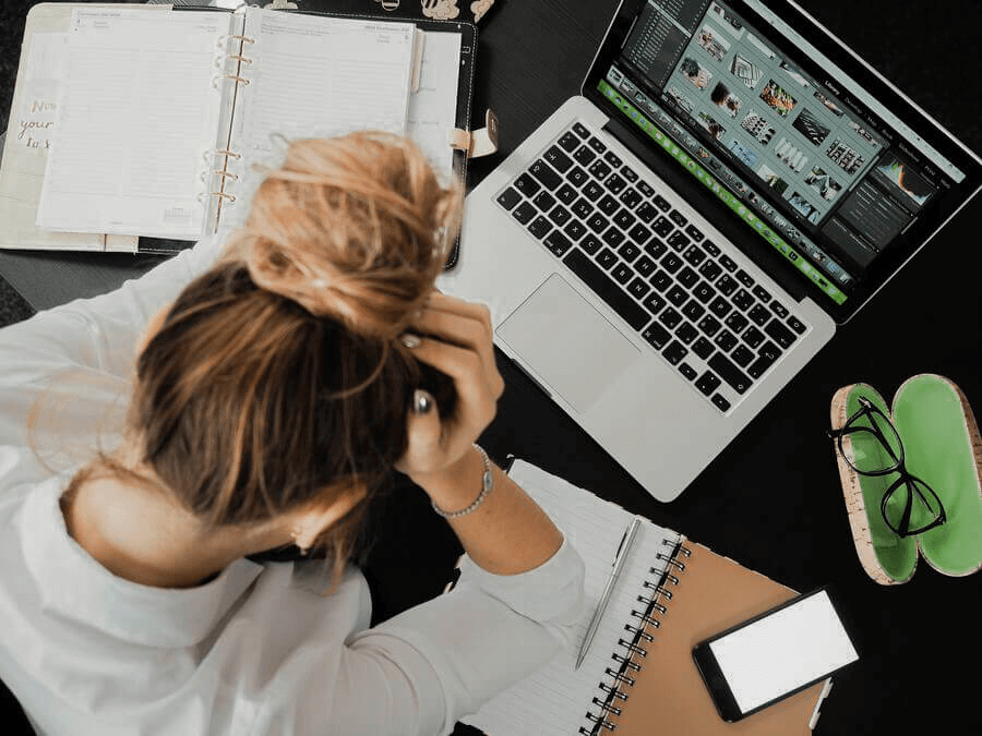 Às vezes dá vontade de desistir de ser produtivo. Mulher sentada em frente ao computador e caderno com a mão na fronte.
